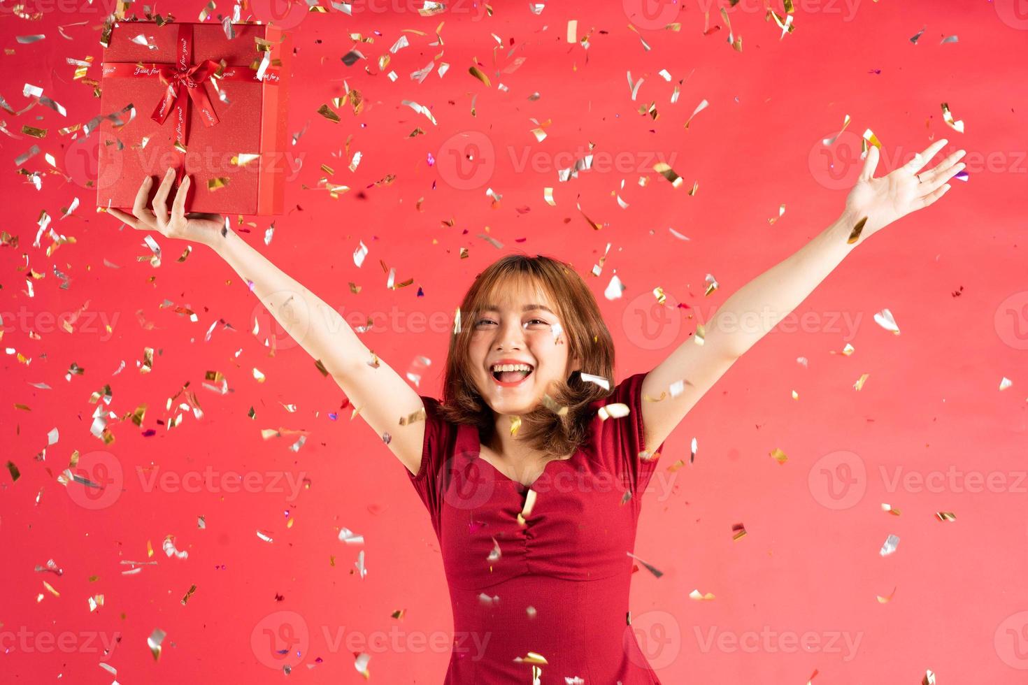 Aziatisch jong meisje in jurk met rode geschenkdoos met vrolijke uitdrukking op achtergrond foto
