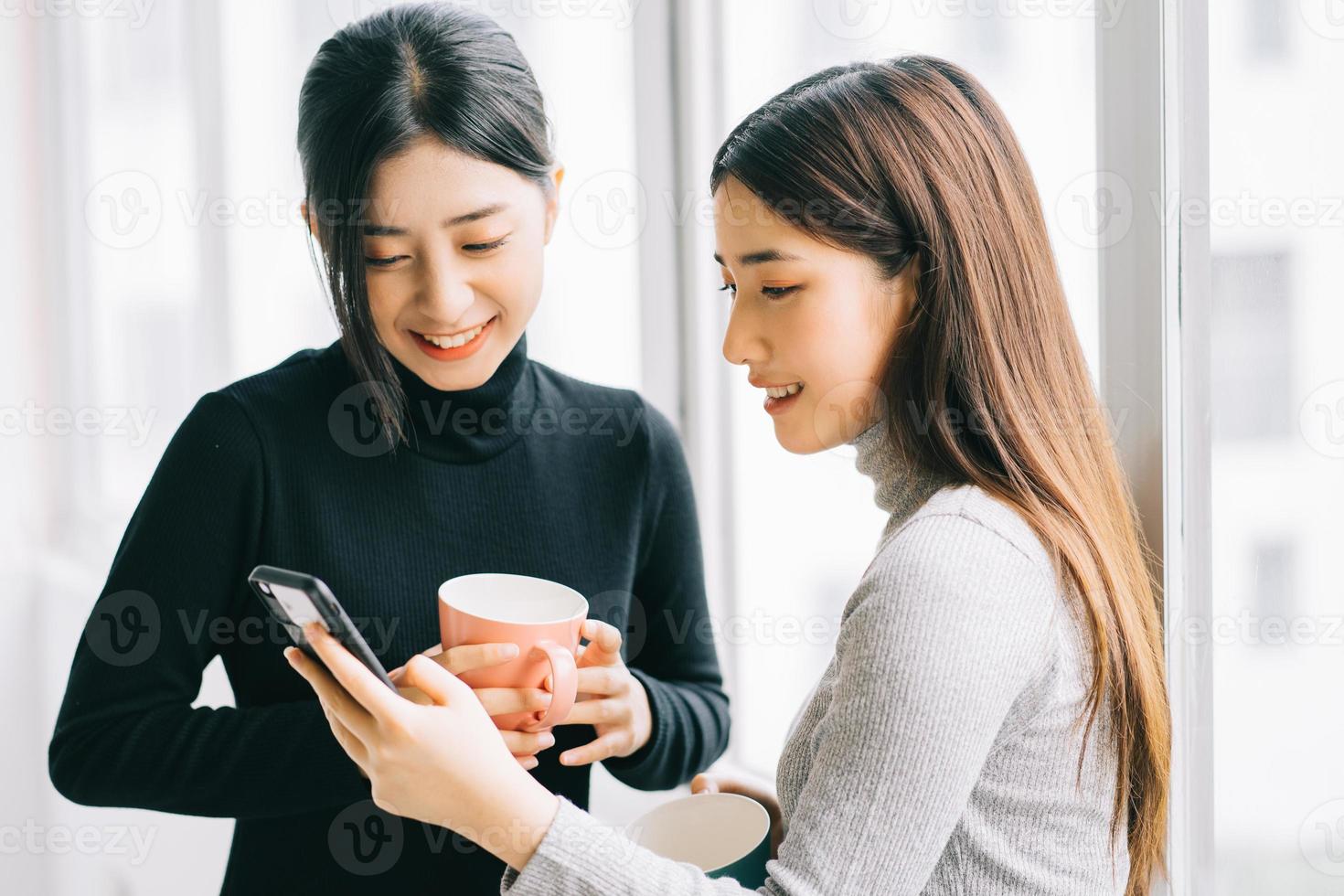 twee Aziatische zakenvrouwen zaten tijdens de pauze bij het raam te kletsen foto