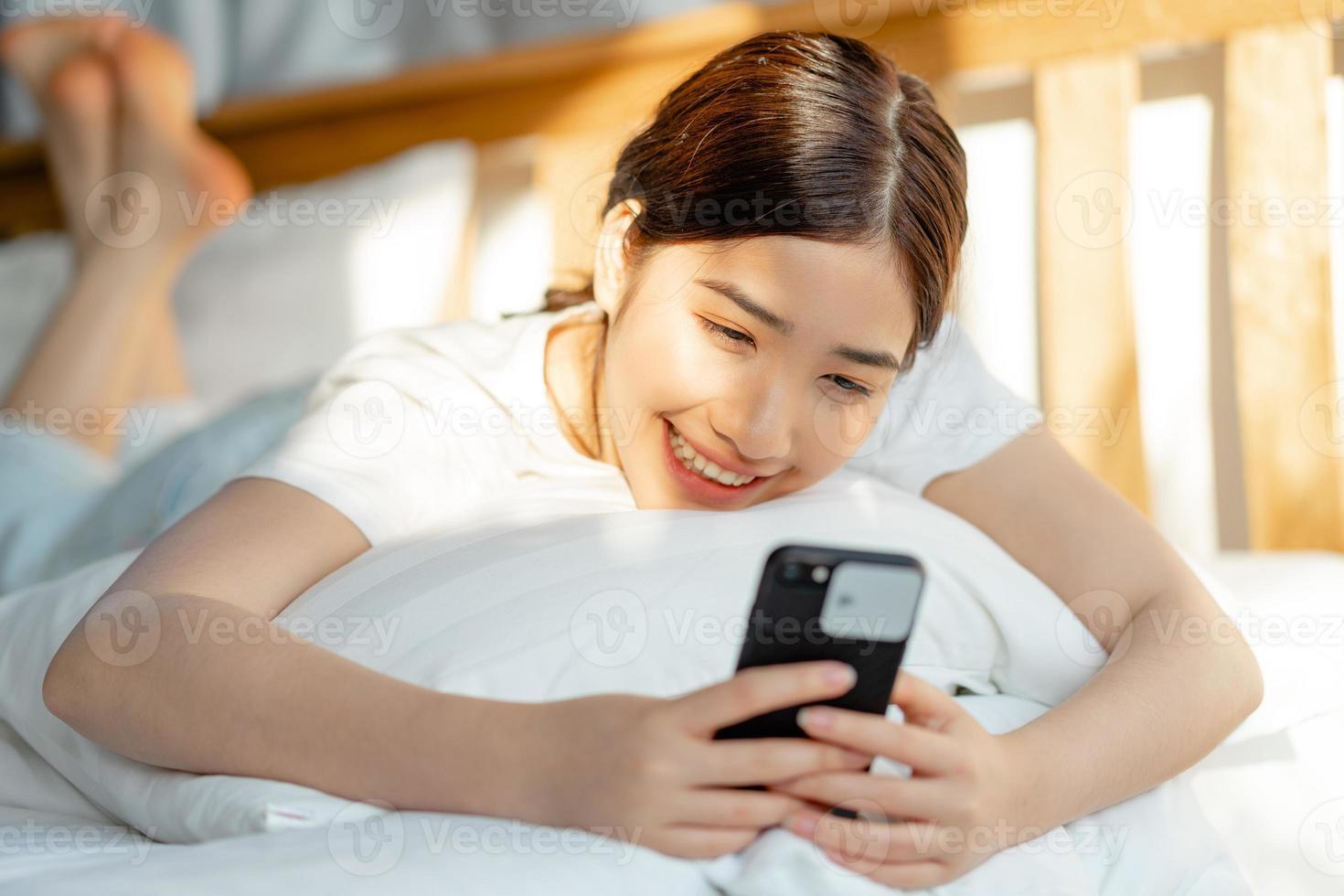 mooie aziatische vrouw die haar telefoon gebruikt als ze net wakker wordt foto