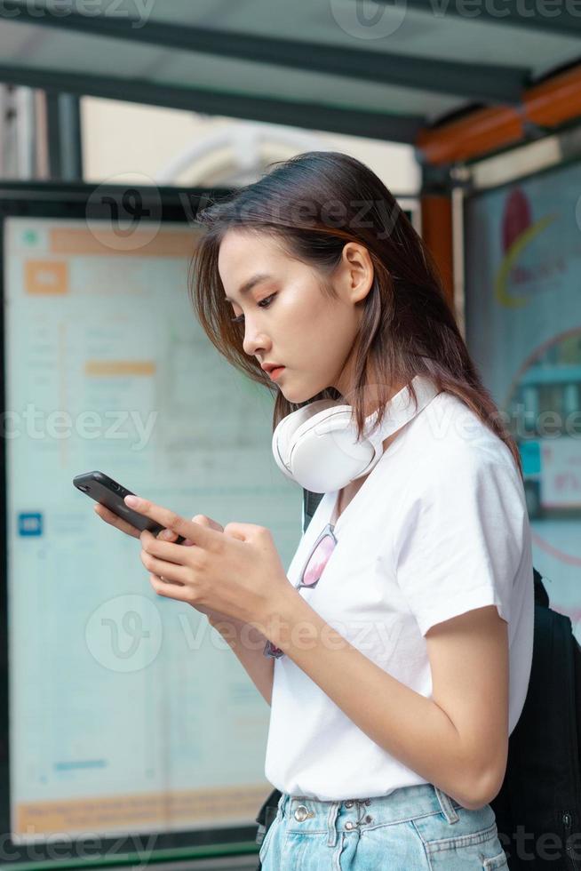mooi Aziatisch meisje gebruikte haar telefoon terwijl ze op de bus wachtte foto