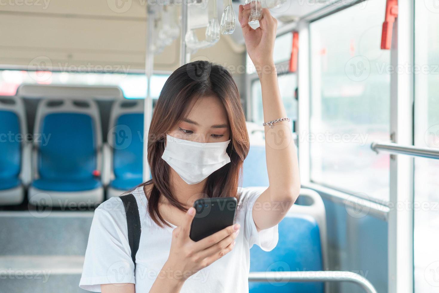 Aziatisch meisje dat een masker draagt tijdens het gebruik van een smartphone in de bus foto