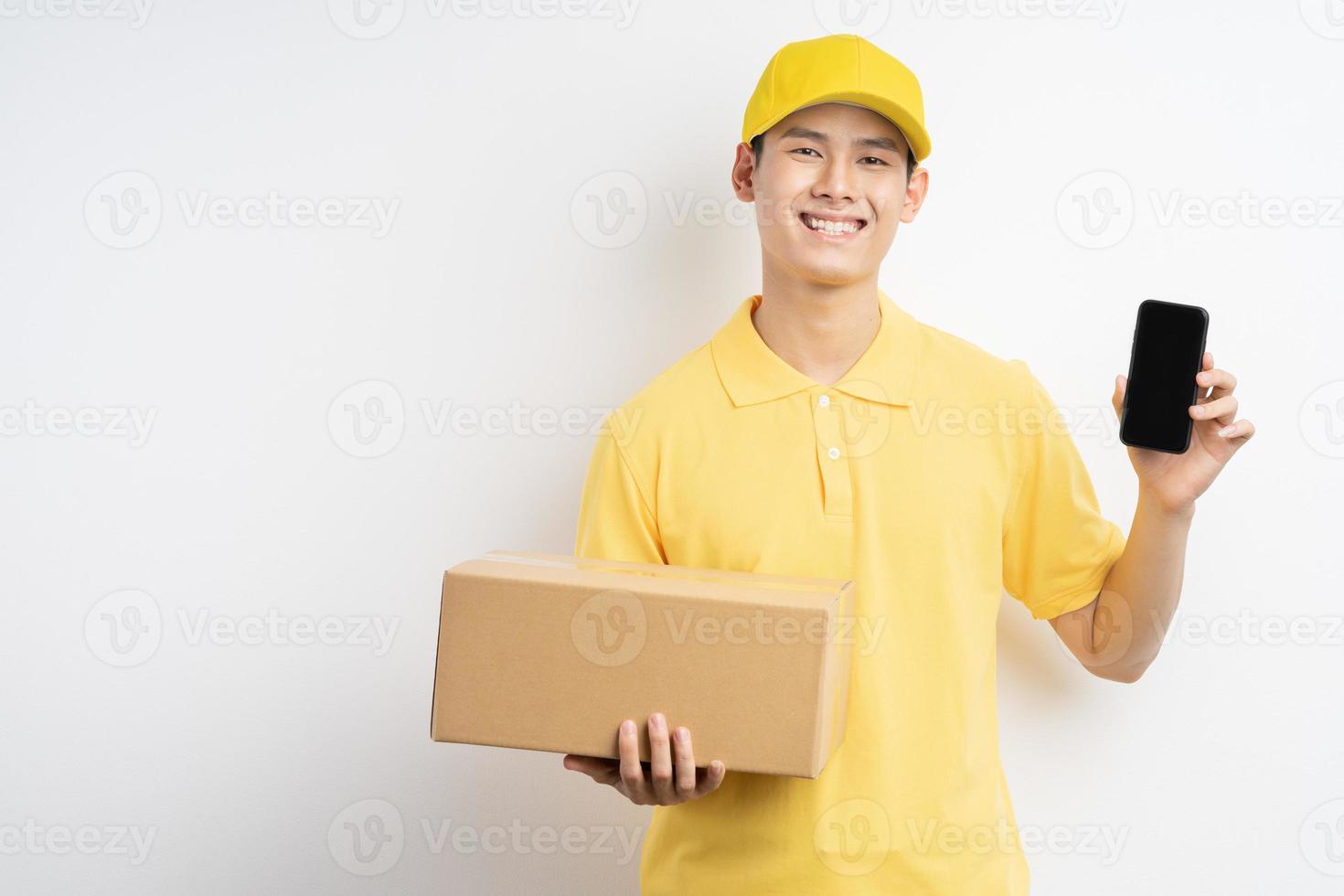 Aziatische man in een geel uniform met een telefoon en een pakket in de ene hand foto