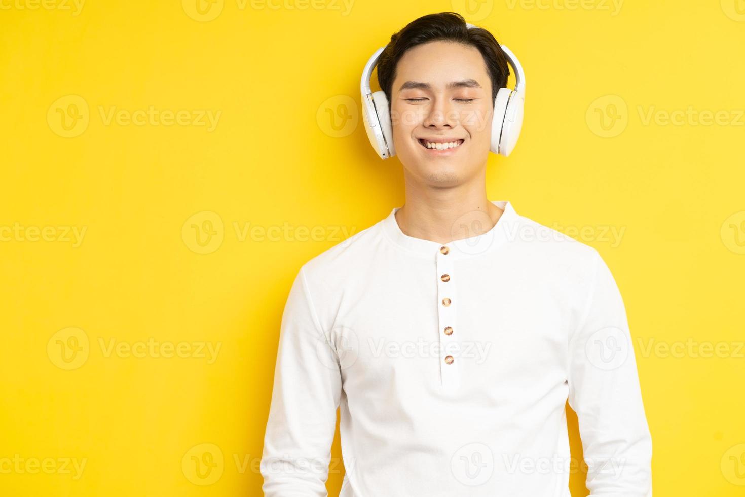 foto van een aziatische man in een wit overhemd die naar muziek luistert met zijn ogen dicht op een gele achtergrond
