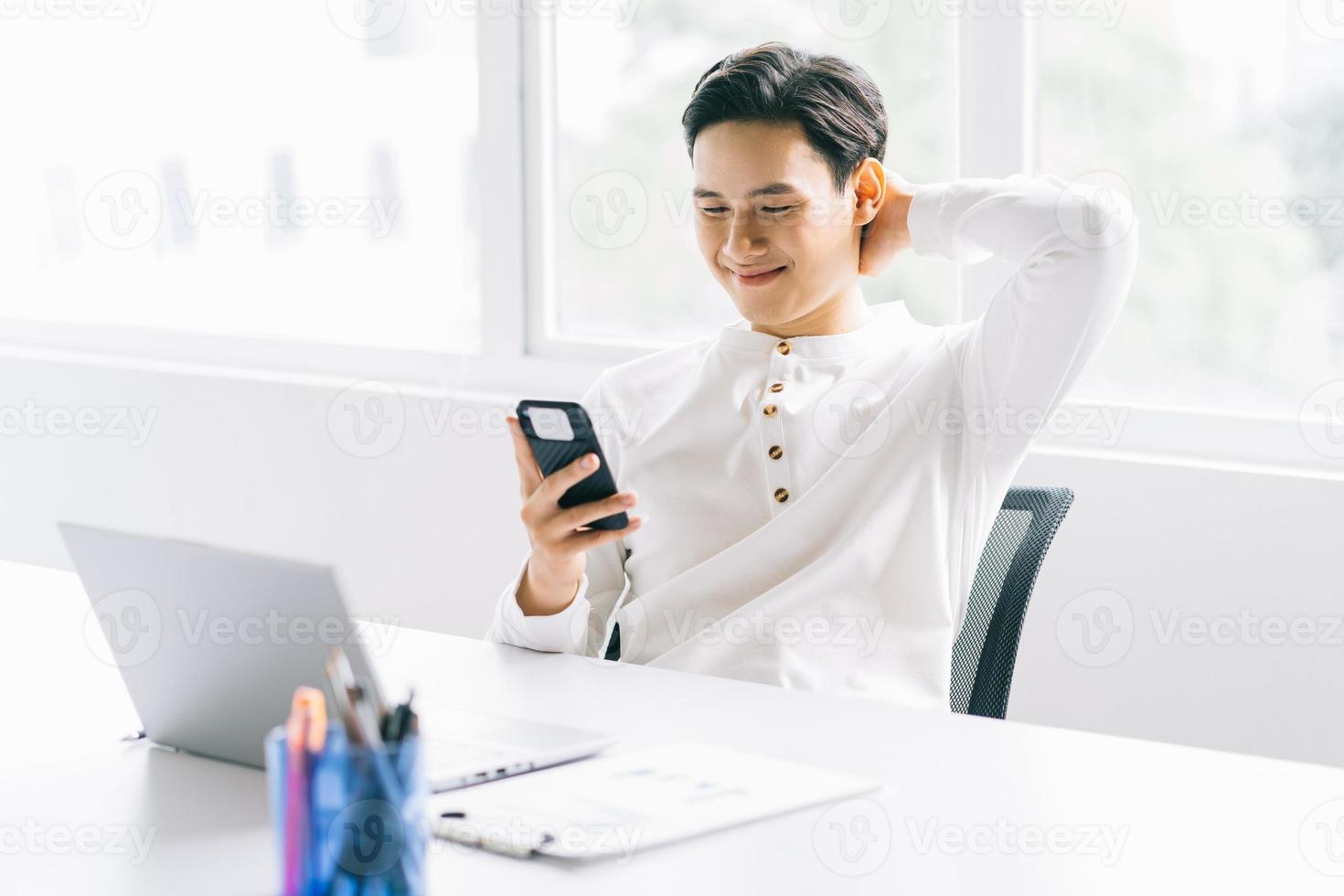 Aziatische zakenman leunt achterover in zijn stoel en gebruikt de telefoon tijdens de pauze foto