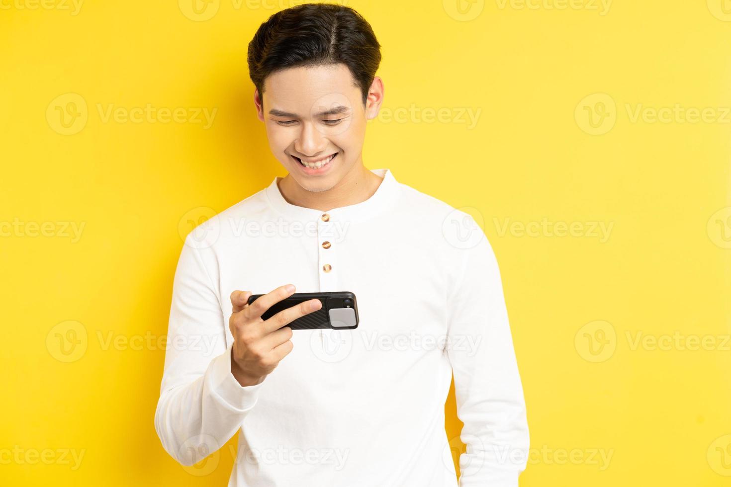 Aziatische man houdt zijn telefoon vast om een film te kijken op een gele achtergrond yellow foto