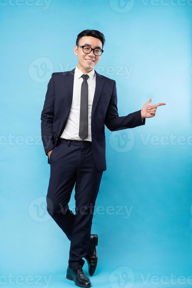 Aziatische zakenman die een pak draagt en op een blauwe achtergrond wijst foto