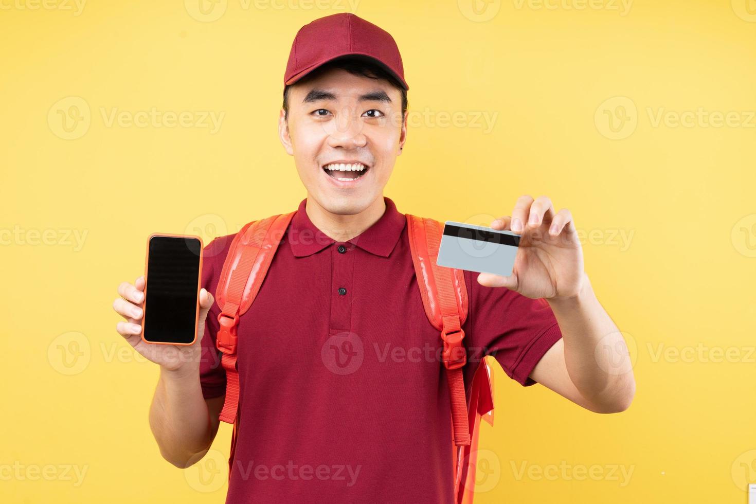 Aziatische bezorger met een rood uniform poserend op gele achtergrond foto