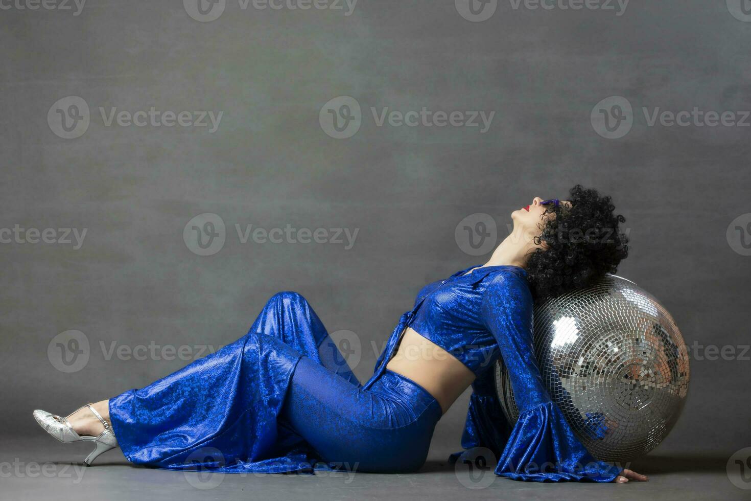 meisje met een disco bal in een afro pruik Aan een grijs achtergrond. disco stijl van de jaren zeventig of jaren tachtig. foto