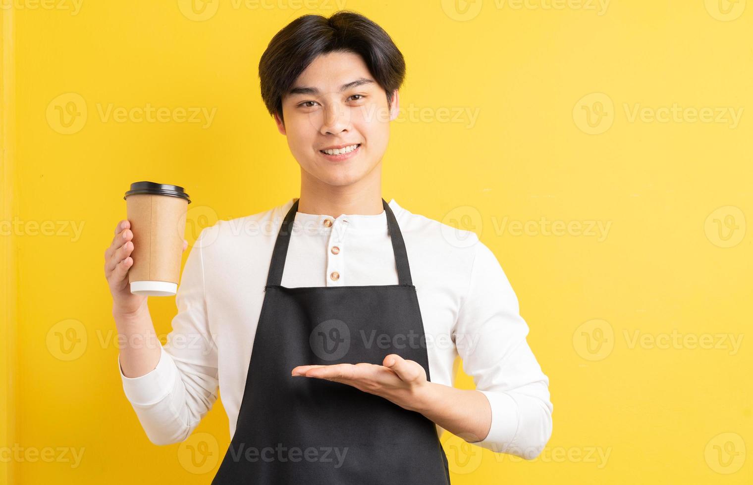 portret van mannelijke ober met papieren beker in de hand op gele achtergrond foto
