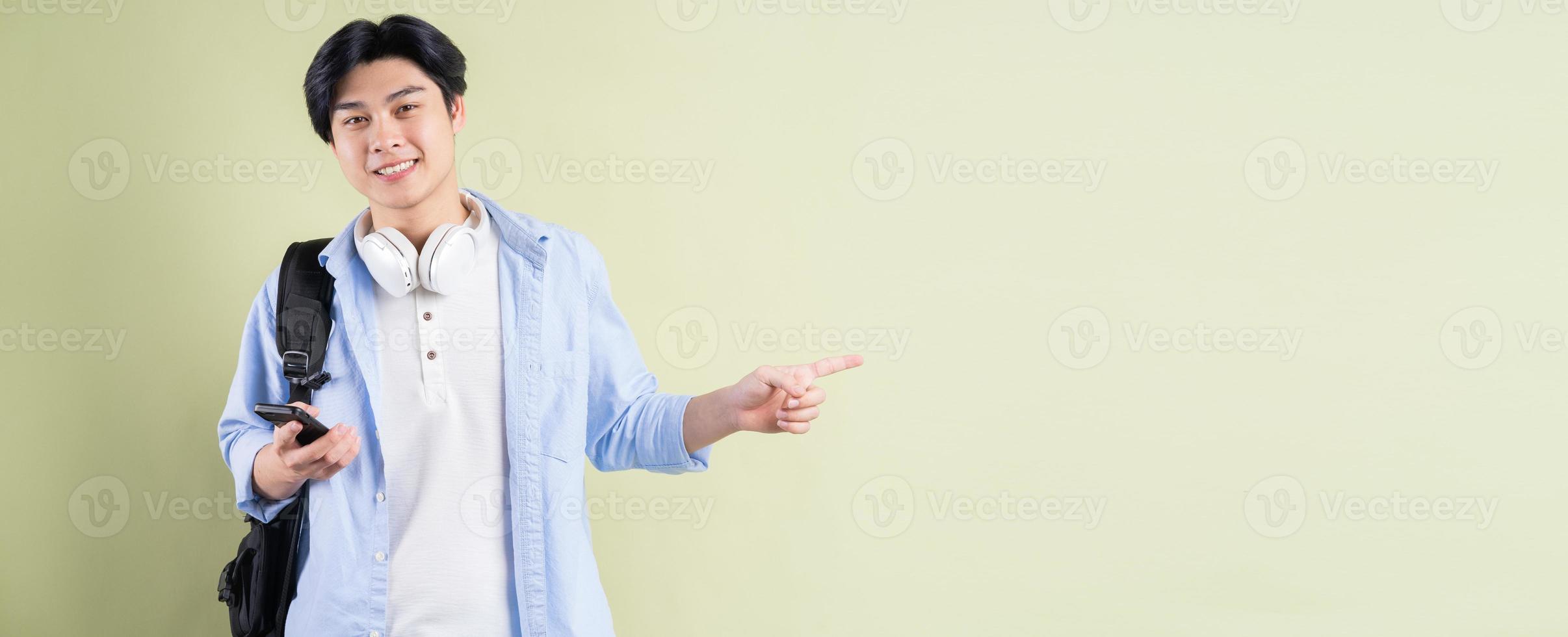 mannelijke Aziatische student lacht en wijst met zijn vinger naar de linkerkant foto