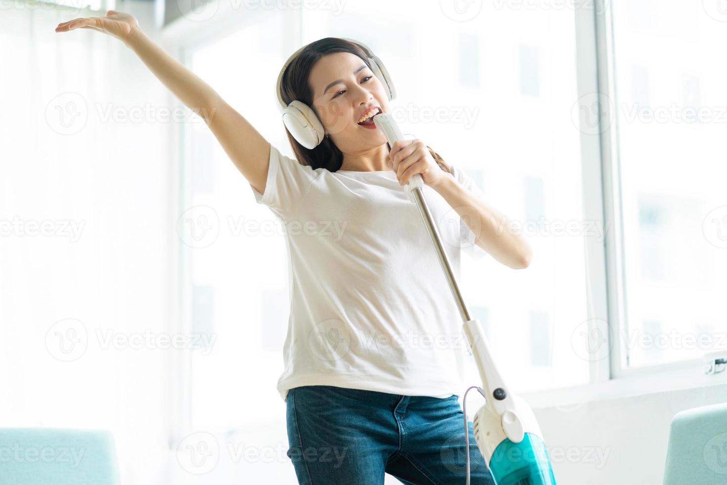 Aziatische vrouw die naar muziek luistert en danst met een stofzuiger a foto