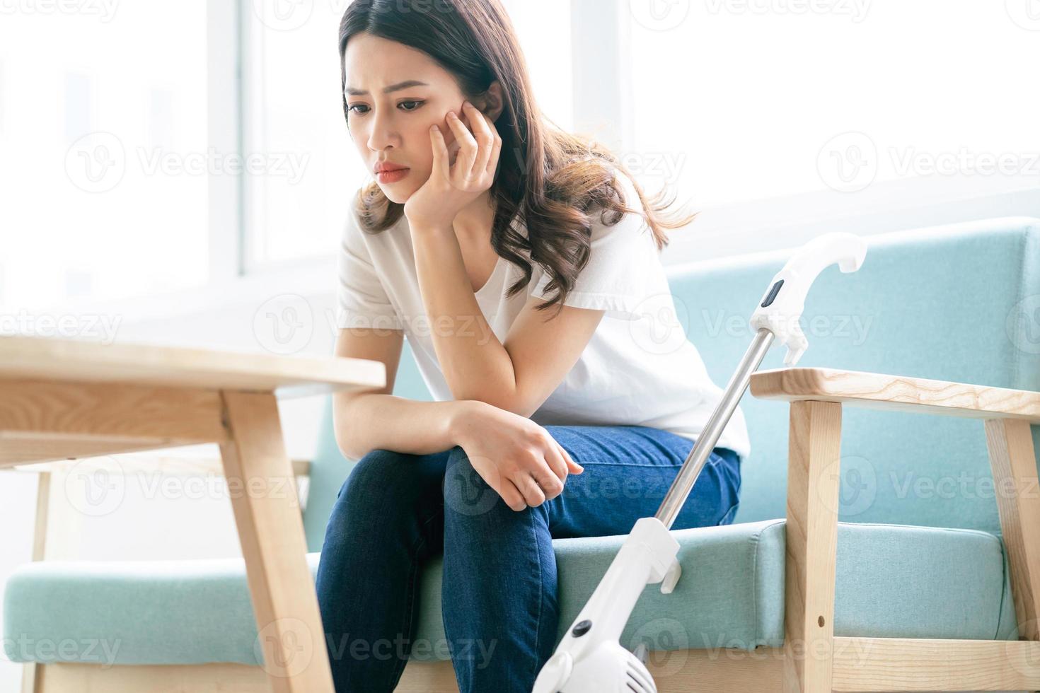 Aziatische vrouw zittend op een stoel met een vermoeide uitdrukking tijdens het schoonmaken van het huis foto