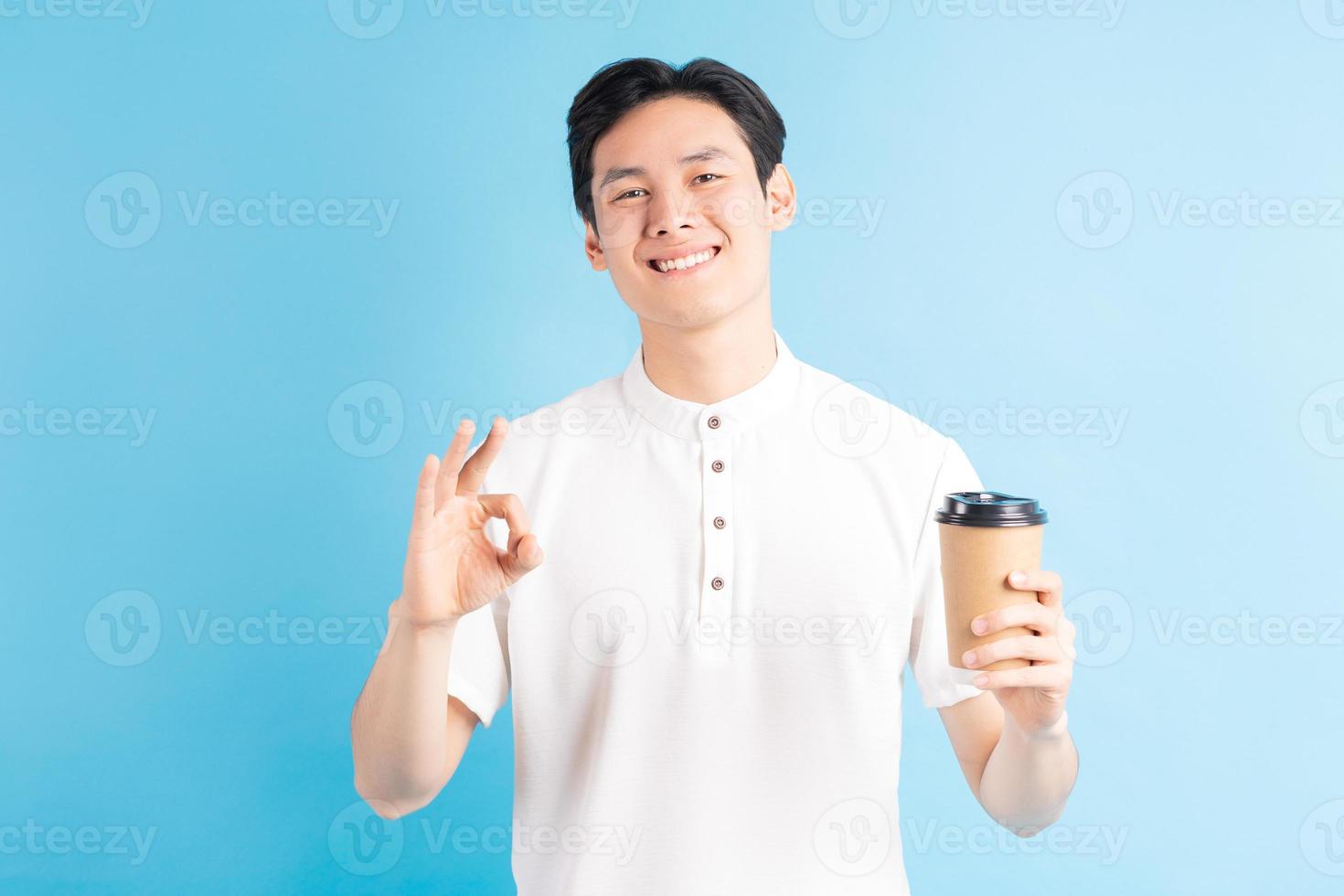 een foto van een knappe Aziatische jongen die een papieren beker in zijn hand houdt en een ok-symbool gebruikt