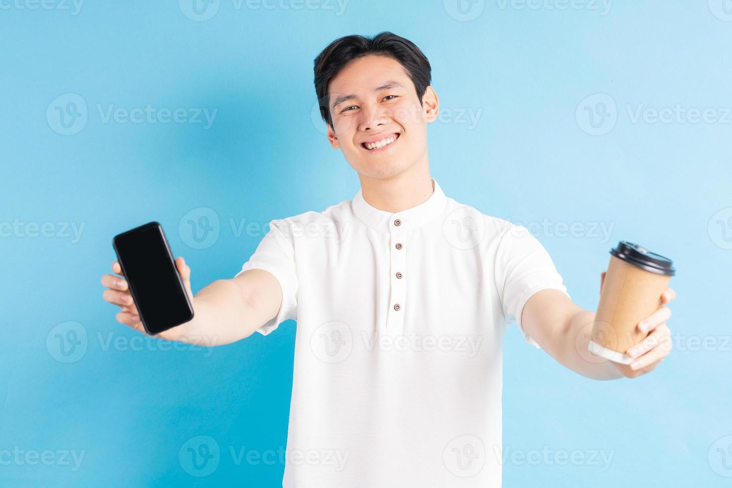 een foto van een knappe Aziatische man die zijn telefoon en papieren beker in zijn hand houdt