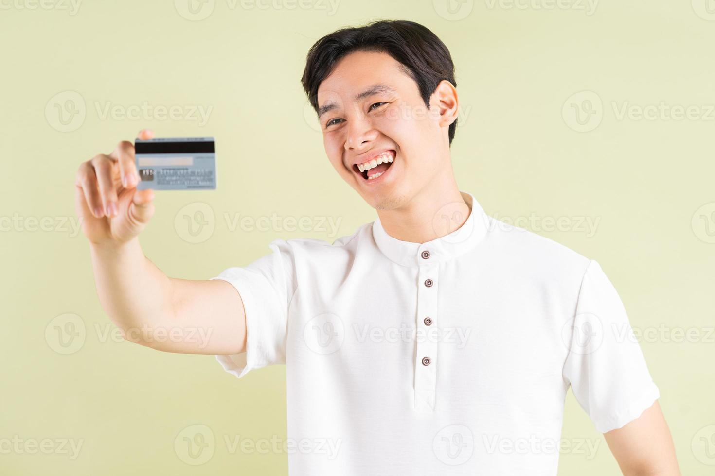 knappe Aziatische zakenman glimlachend en kijkend naar de creditcard in zijn hand foto