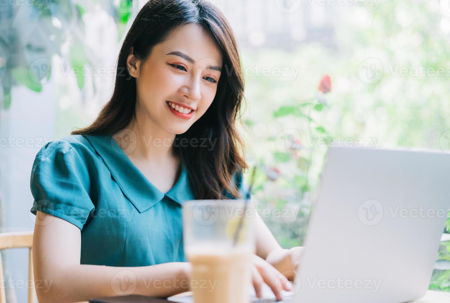 jonge aziatische vrouw die laptop met behulp van bij coffeeshop foto
