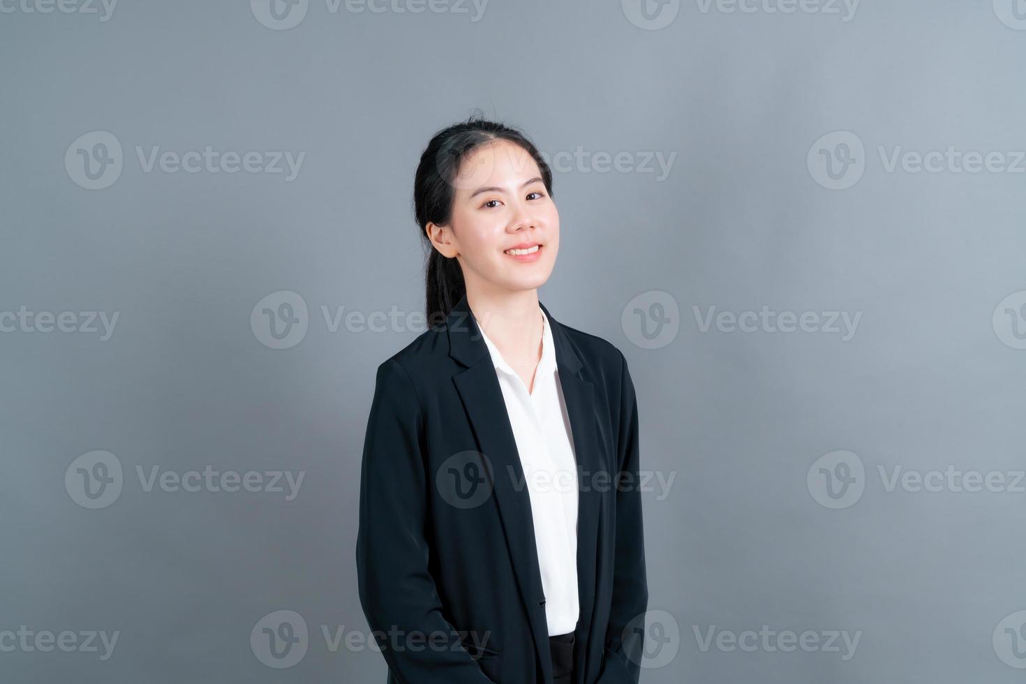 gelukkige aziatische vrouw met blij gezicht in kantoorkleren op grijze achtergrond foto