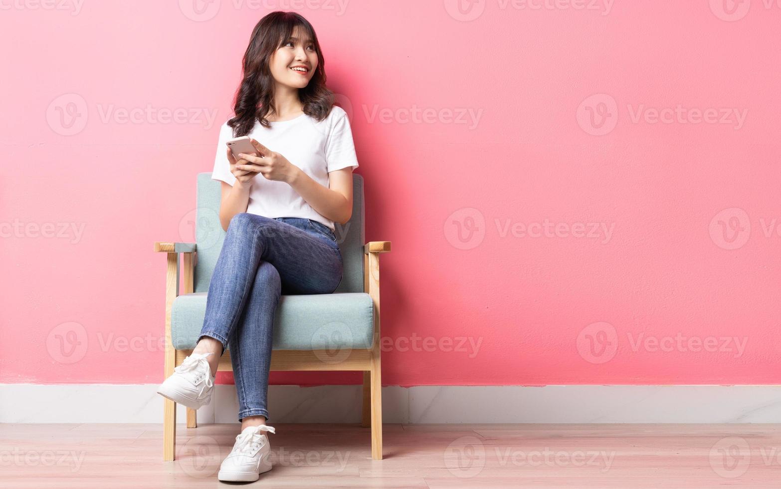Aziatische vrouw zittend op de bank met behulp van haar telefoon met een gelukkige uitdrukking foto