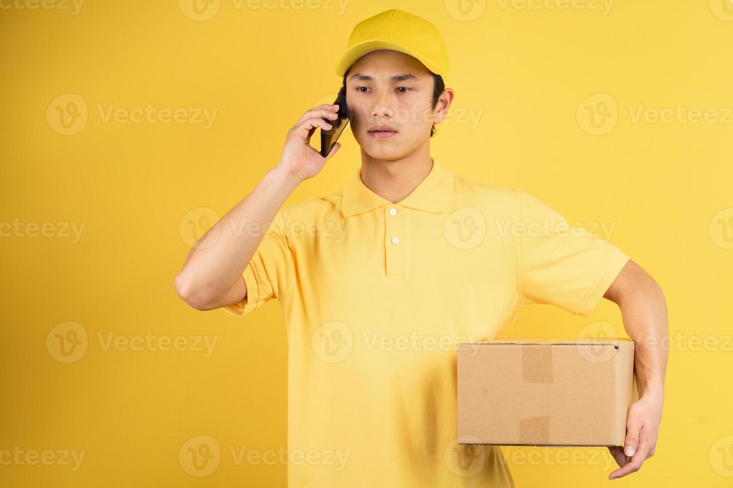 portret van bezorger die een vrachtdoos vasthoudt en naar de telefoon luistert op gele achtergrond foto