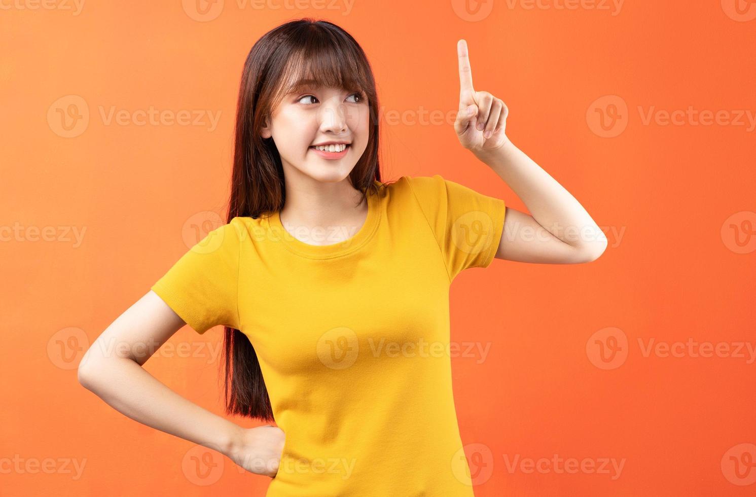 afbeelding van een jong Aziatisch meisje met een geel t-shirt op een oranje achtergrond foto