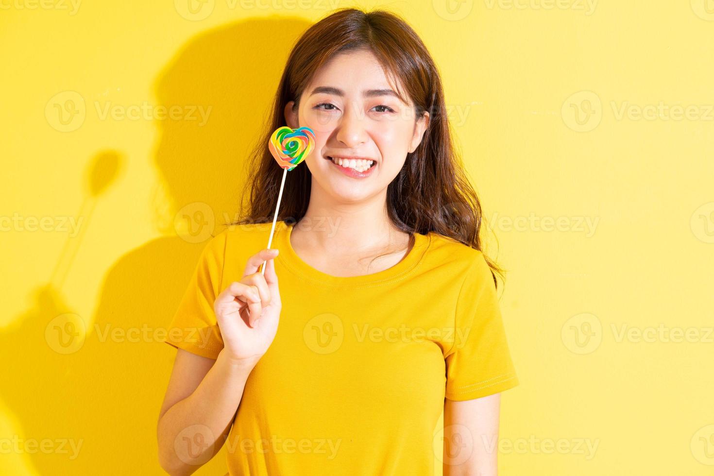 jonge aziatische vrouw die lolly op gele achtergrond eet foto