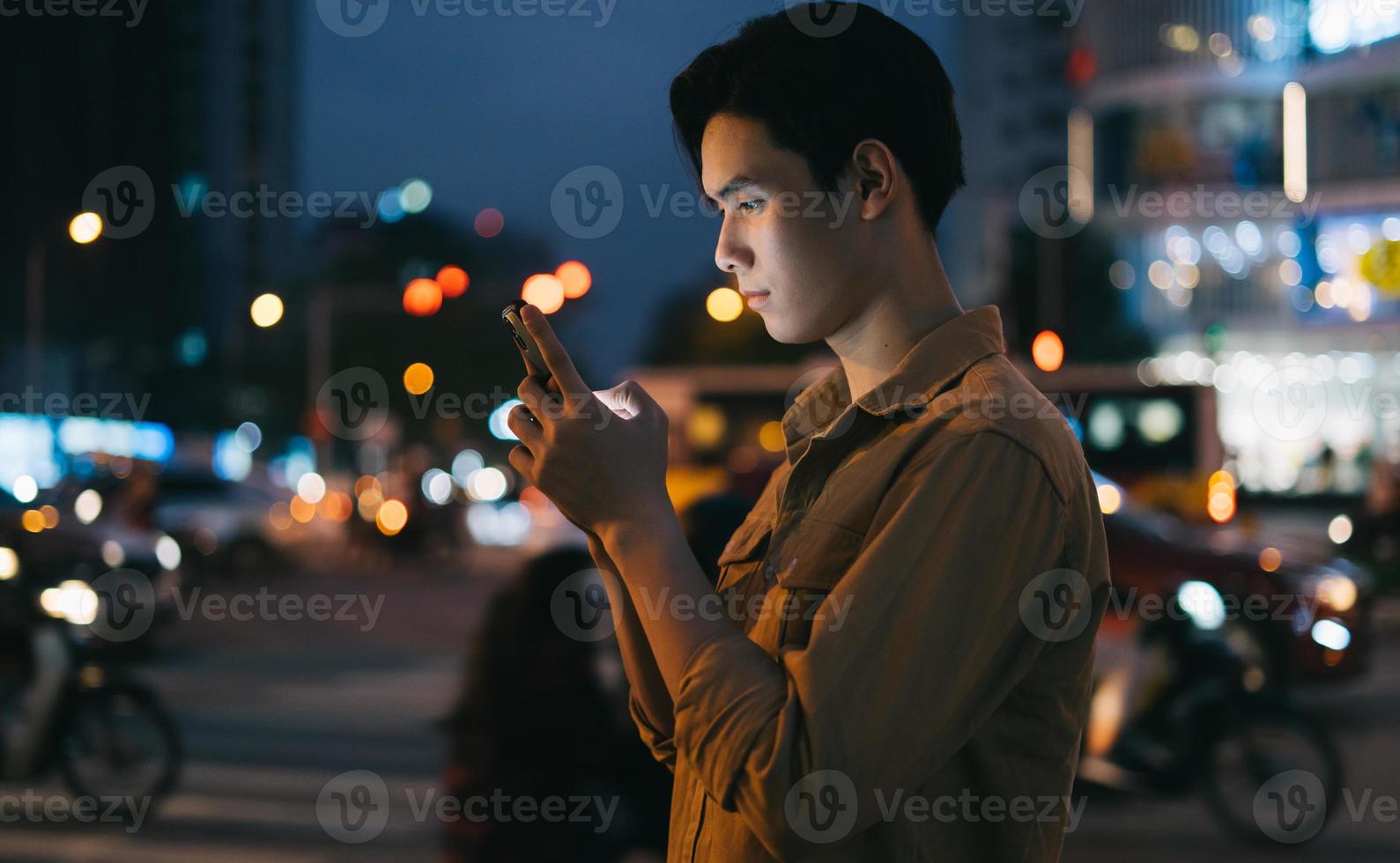 jonge aziatische man gebruikt zijn telefoon terwijl hij 's nachts op straat loopt foto