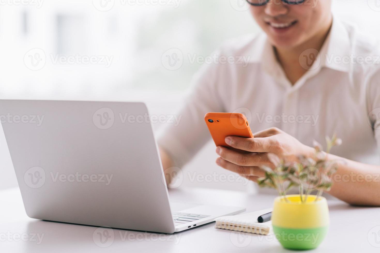 jonge Aziatische zakenman die smartphone en laptop op kantoor gebruikt foto