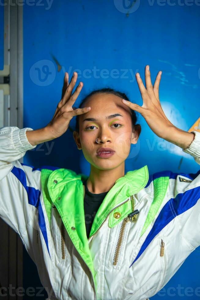 een homo Aziatisch Mens poseren in een trainingspak in voorkant van een blauw kastje foto