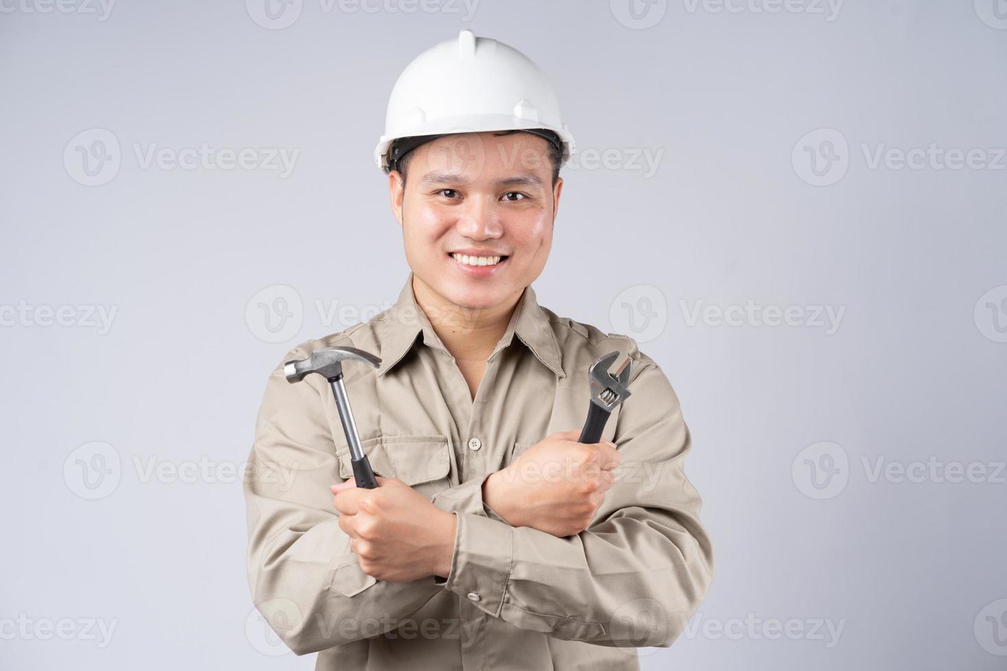 Aziatische reparateur permanent met gevouwen armen op grijze achtergrond foto