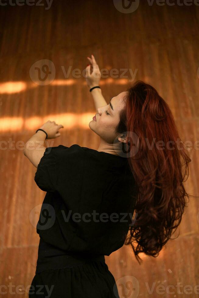 een Aziatisch Mens met lang en rood haar- poseren in een zwart overhemd in een houten huis foto