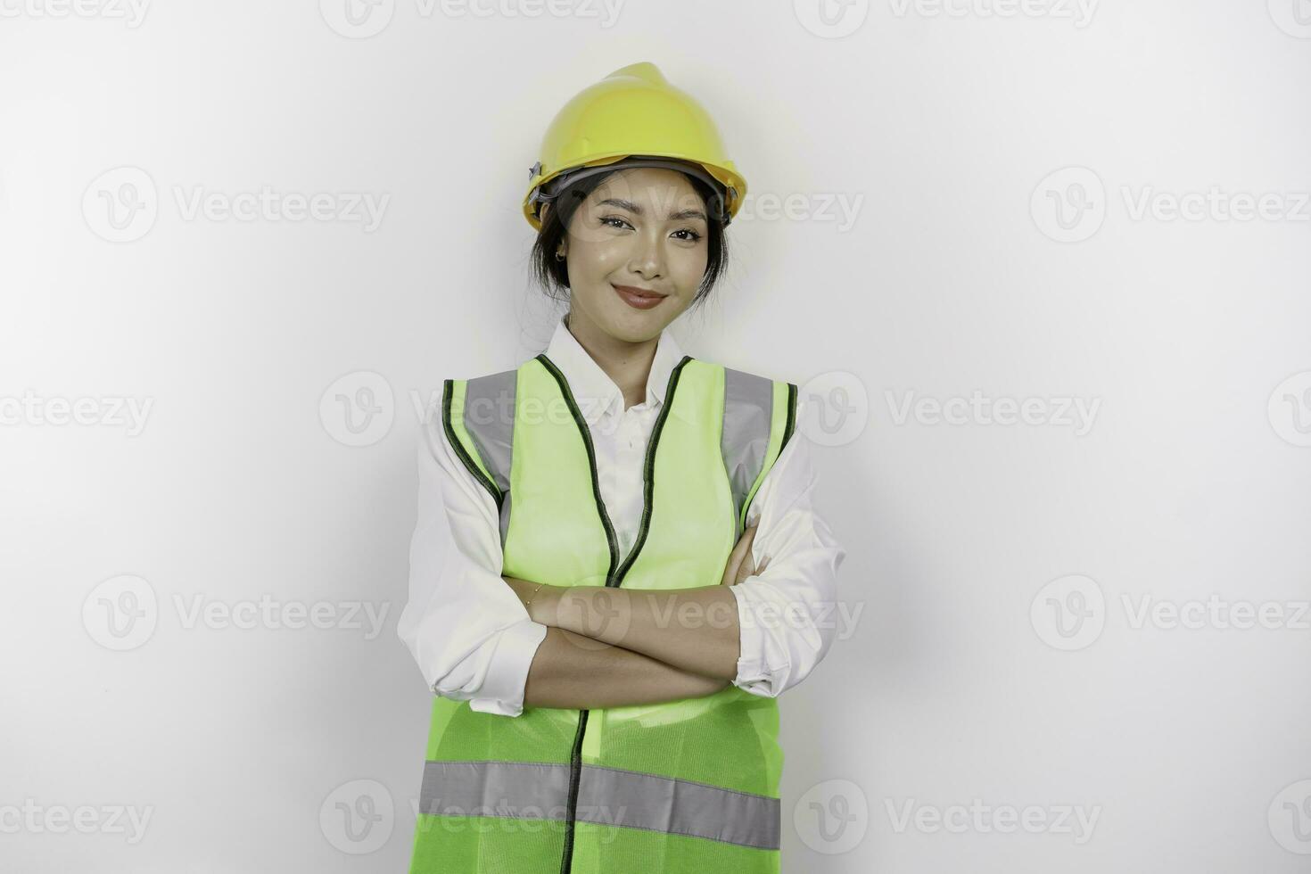 glimlachen Aziatisch vrouw arbeid arbeider in industrie fabriek, poseren met armen gevouwen, vervelend geel veiligheid helm, groen hesje en uniform, geïsoleerd wit achtergrond. foto