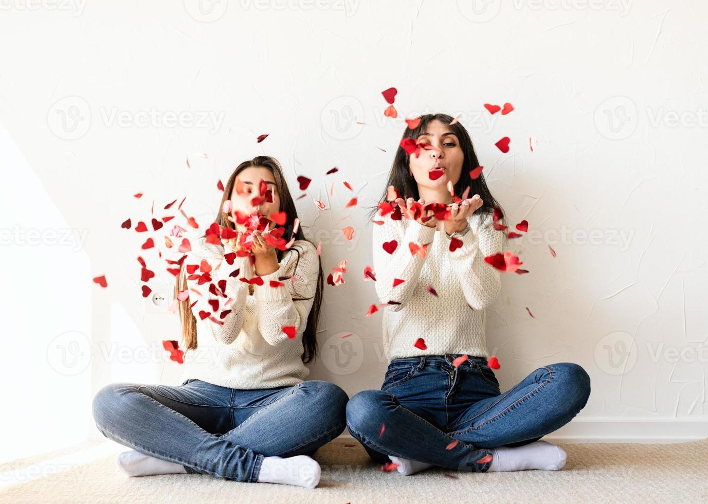 twee beste vrienden die thuis plezier hebben en rode confetti blazen foto