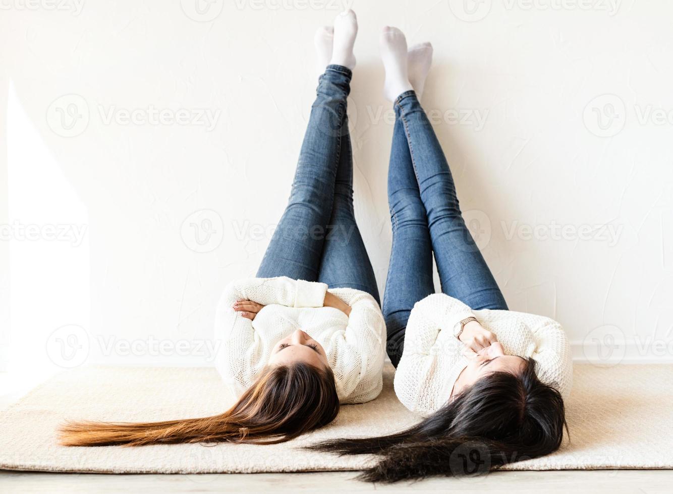 twee vrouwen die op het tapijt liggen, benen omhoog en plezier hebben foto