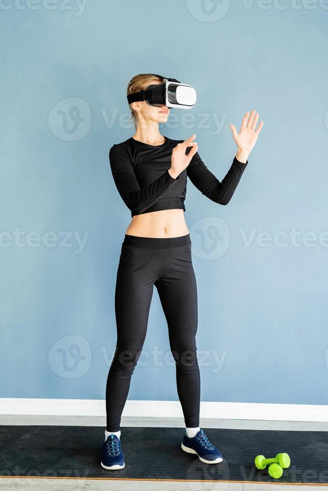 jonge blonde vrouw in sportkleding met een virtual reality-bril die op een fitnessmat staat met behulp van vr interactief menu foto