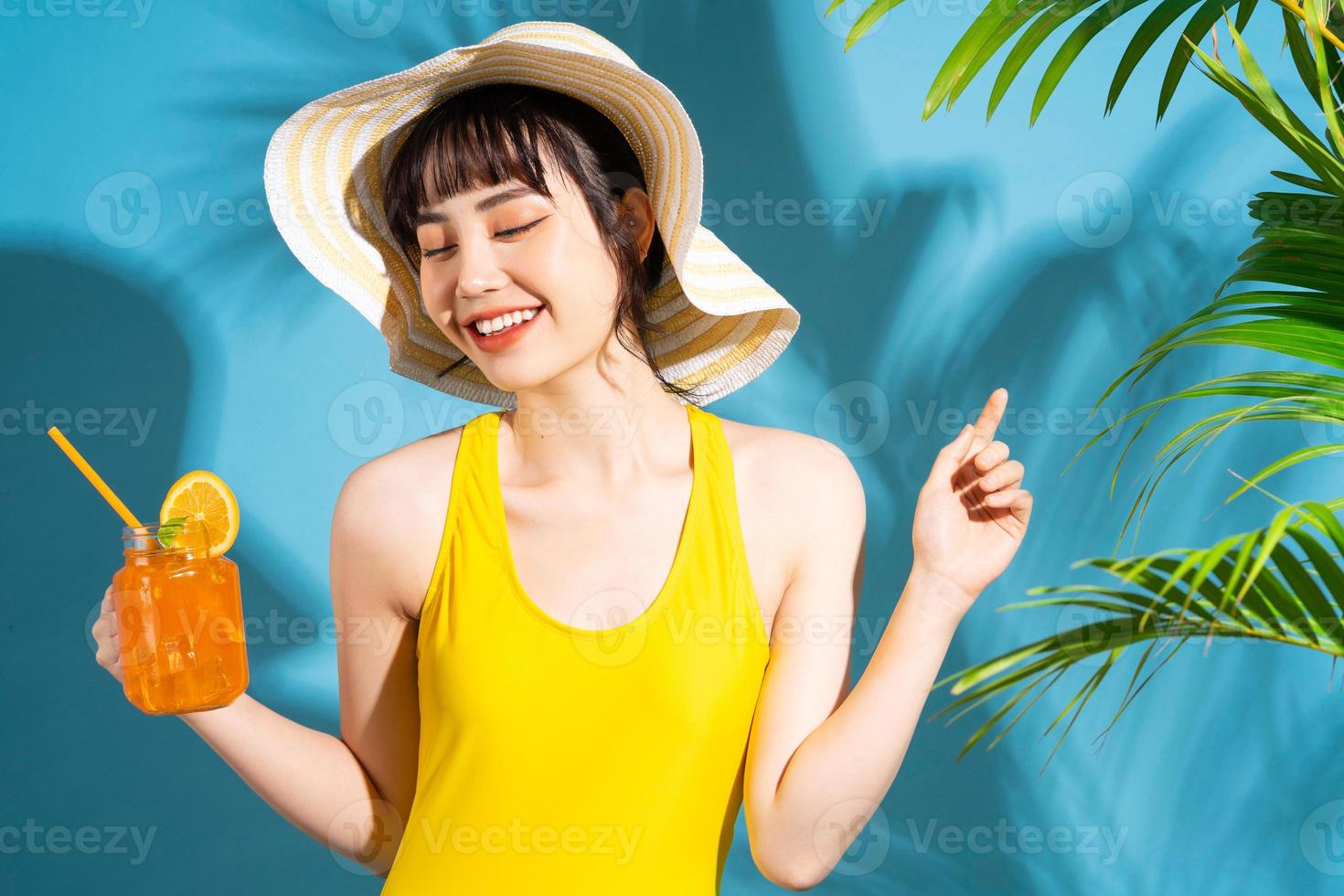 mooie aziatische vrouw die gele jumpsuit op blauwe achtergrond draagt en sap drinkt, zomerconcept foto