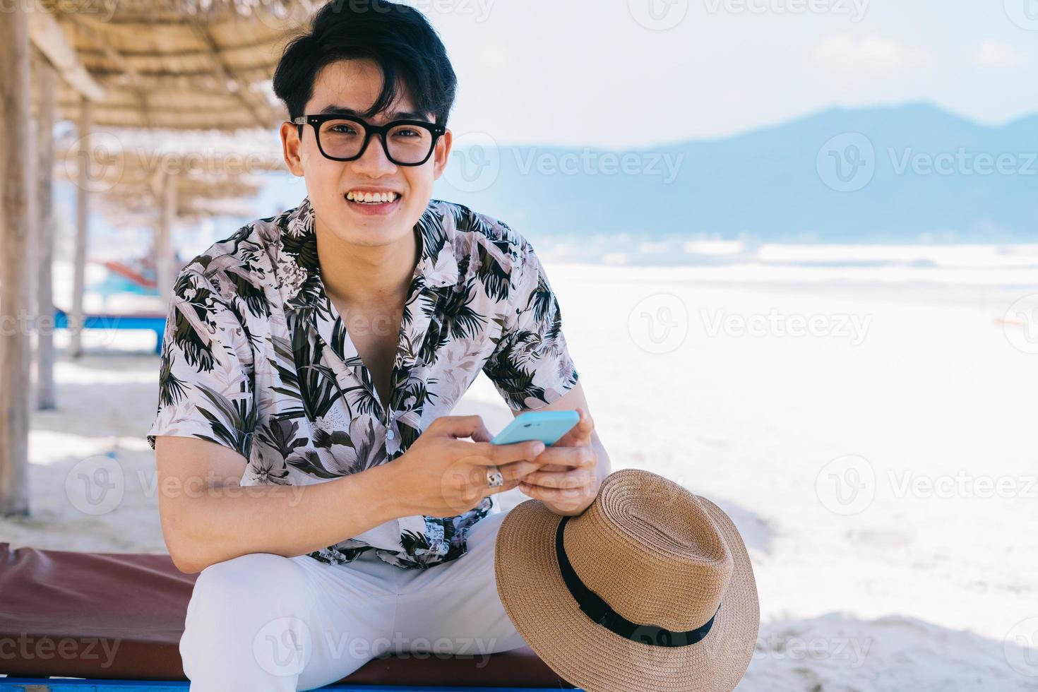 jonge Aziatische man met smartphone op het strand the foto