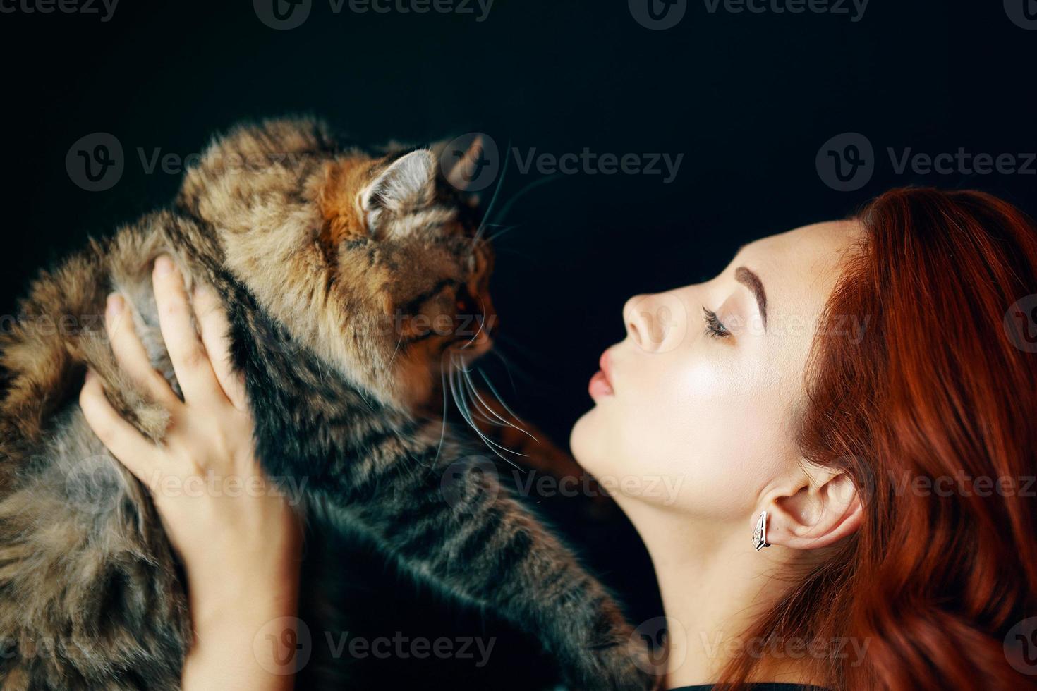 roodharig meisje houdt pluizige kat op zwarte achtergrond. foto