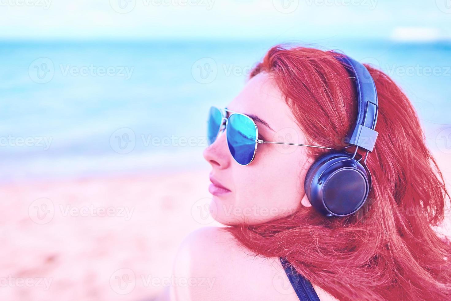 mooie vrouw in zonnebril luisteren naar muziek op het strand. foto
