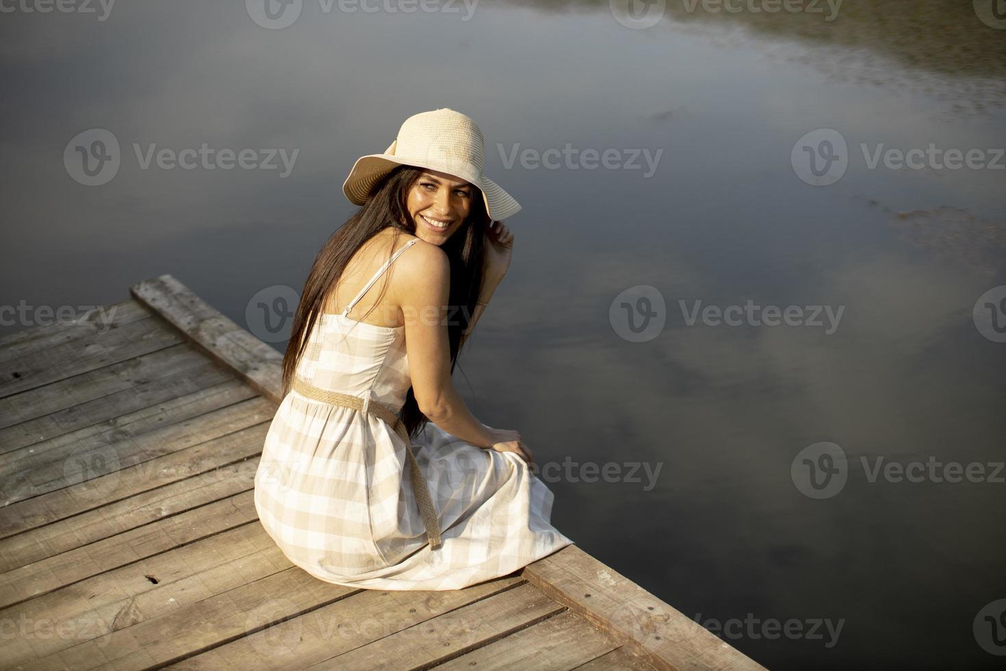 ontspannende jonge vrouw op houten pier aan het meer foto