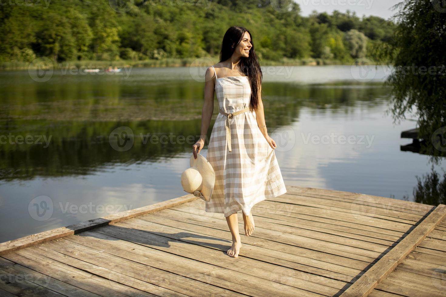 ontspannende jonge vrouw die op een houten pier aan het meer staat foto