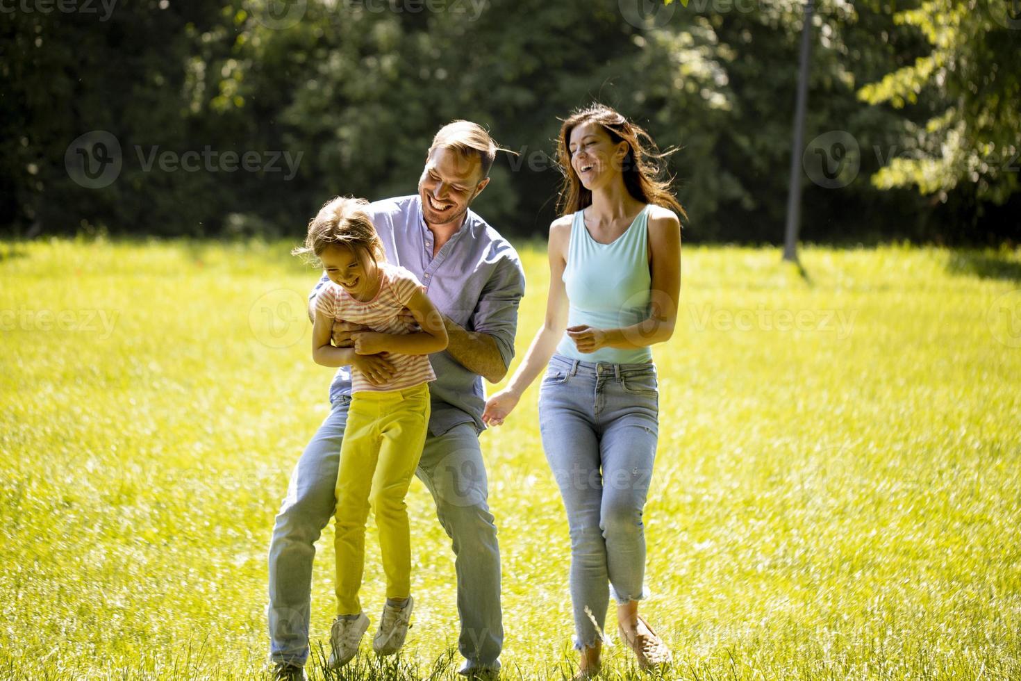gelukkig jong gezin met schattig dochtertje dat op een zonnige dag in het park rent foto
