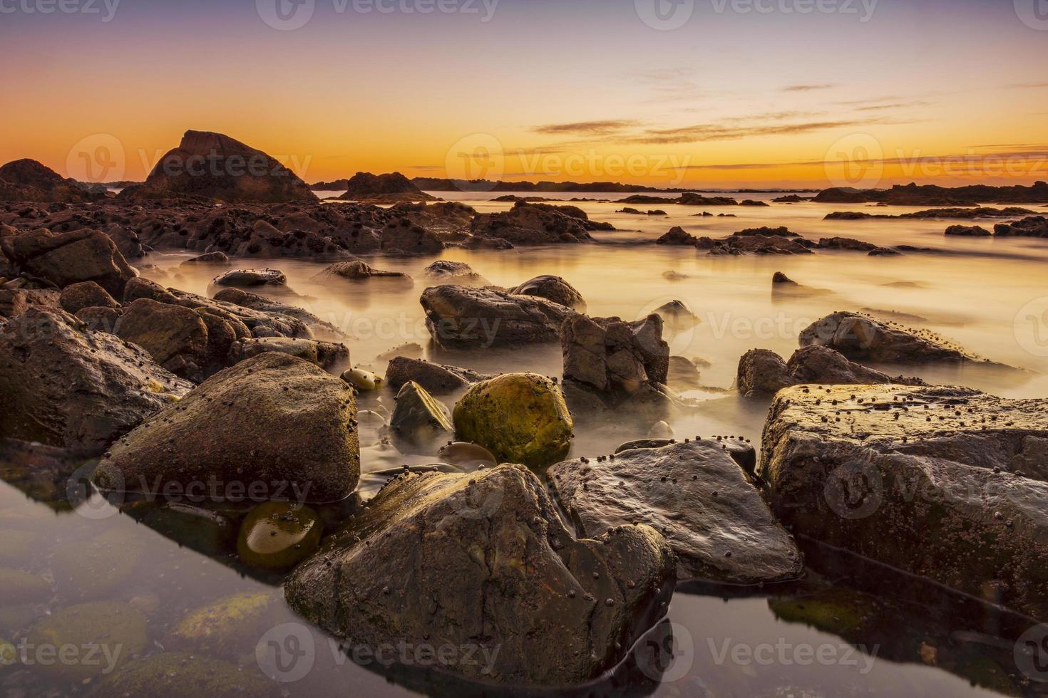 rotsachtig strand met gouden kleuren bij zonsondergang foto