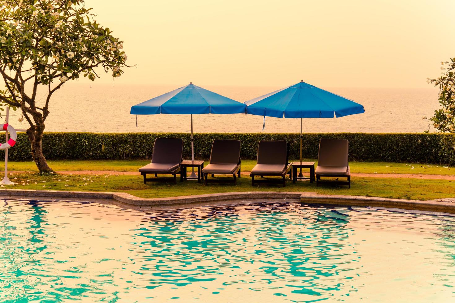 strandstoelen of zwembadbedden met parasols rond het zwembad bij zonsondergang sunset foto