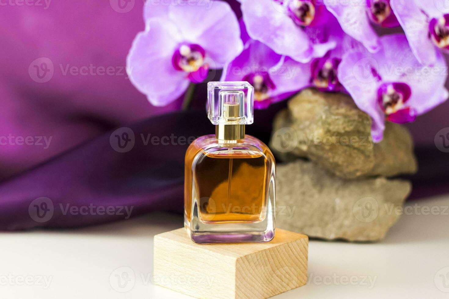 de parfum fles staat Aan een houten voetstuk tegen een achtergrond van steen en mooi orchideeën. elegant uiterlijk van de Product, lay-out, persoonlijkheid. banier, een plaats voor de tekst. foto