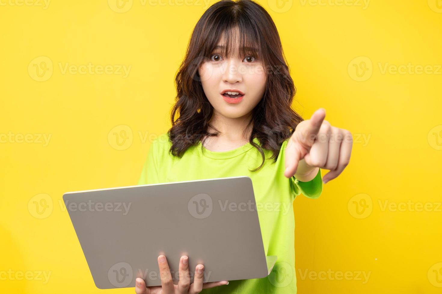 jonge aziatische vrouw die laptop op gele achtergrond gebruikt foto