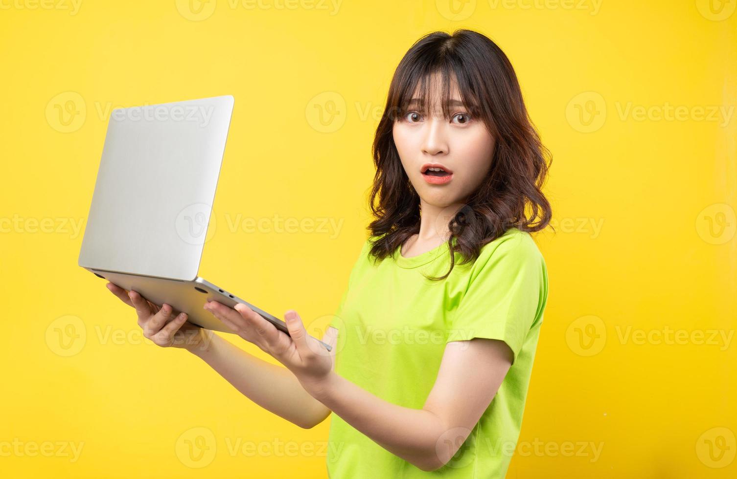 jonge aziatische vrouw die laptop op gele achtergrond gebruikt foto