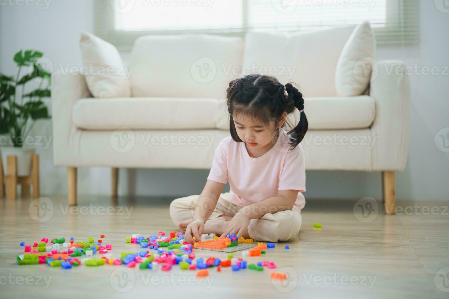 blij Aziatisch meisje gelukkig en glimlachen spelen kleurrijk Lego speelgoed, zittend Aan de leven kamer vloer, creatief spelen met Lego, gebouw kleurrijk structuren creativiteit stel je voor. aan het leren onderwijs. foto