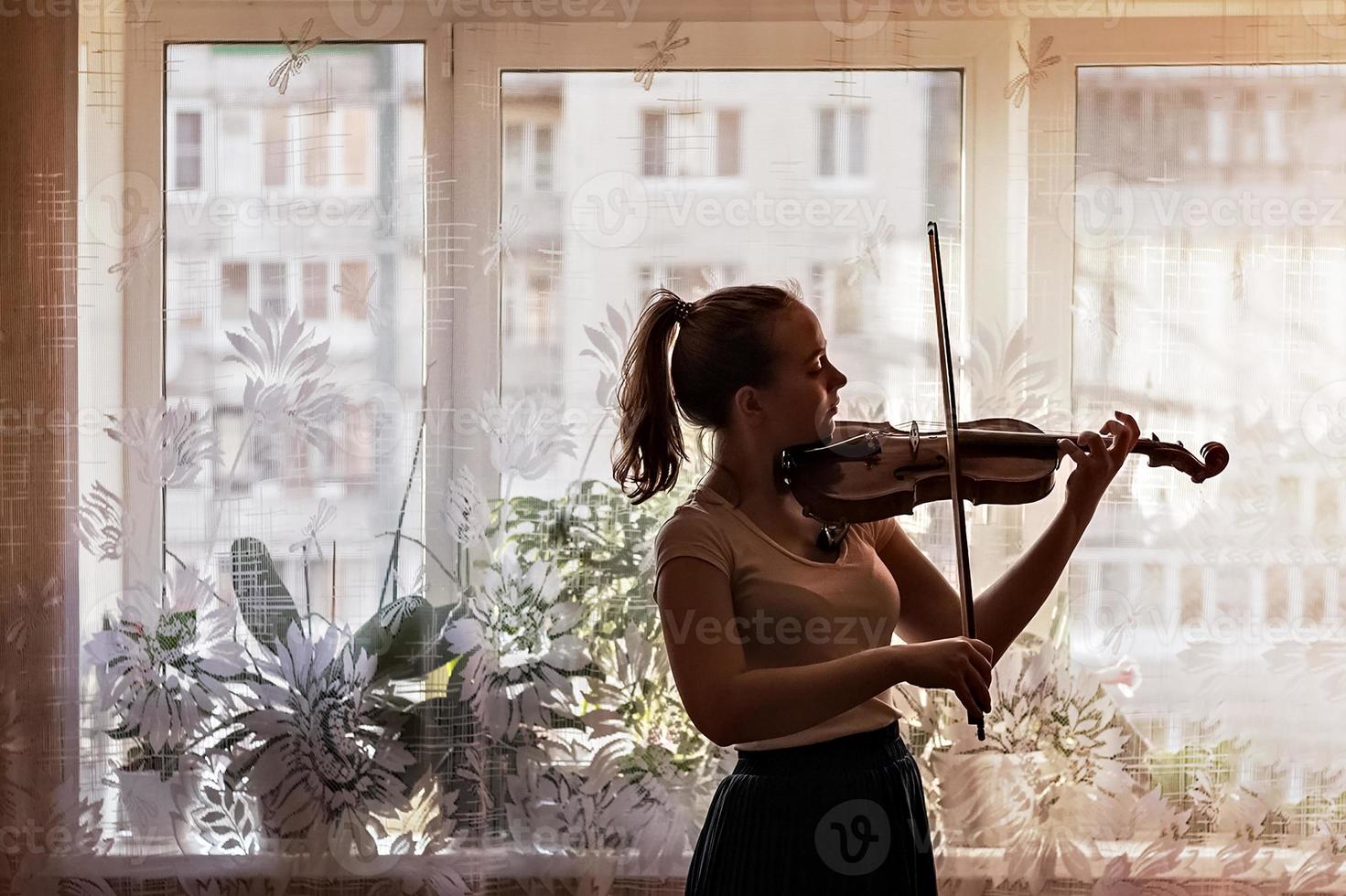 silhouet van een jong meisje, een muzikant. viool spelen op de achtergrond van het raam foto