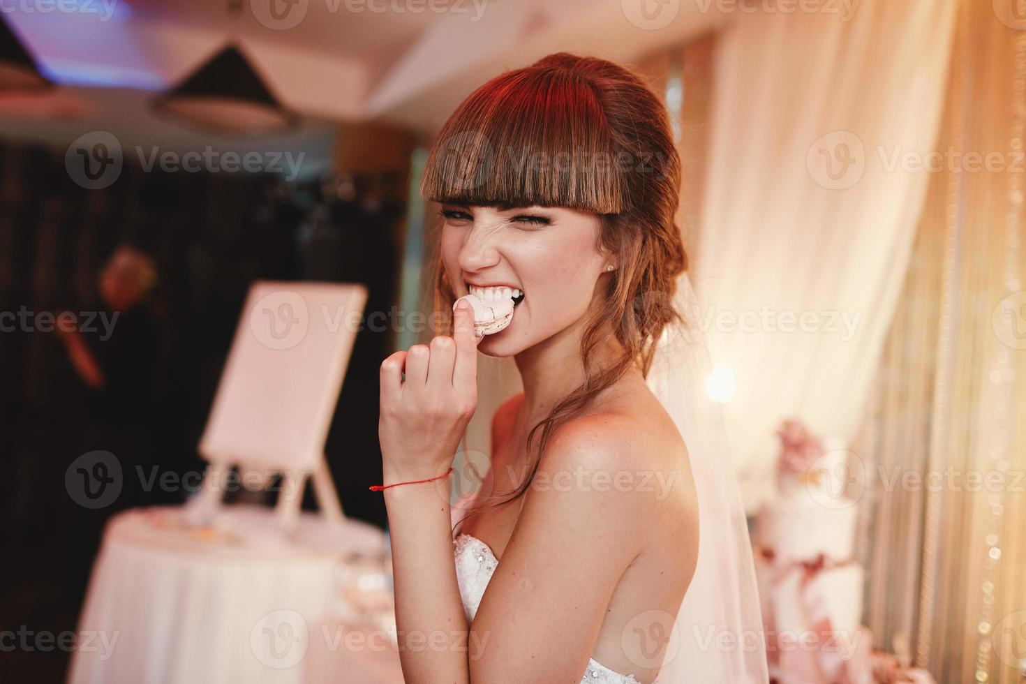 portret van een stijlvolle, vrolijke bruid die een frans macaroondessert eet. bruiloft en vakantie concept foto