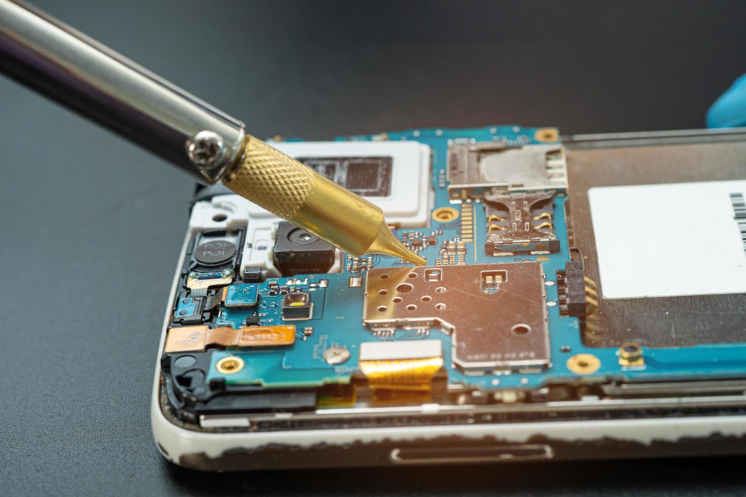 technicus die binnenkant van mobiele telefoon repareert door soldeerbout. geïntegreerde schakeling. het concept van gegevens, hardware, technologie. foto